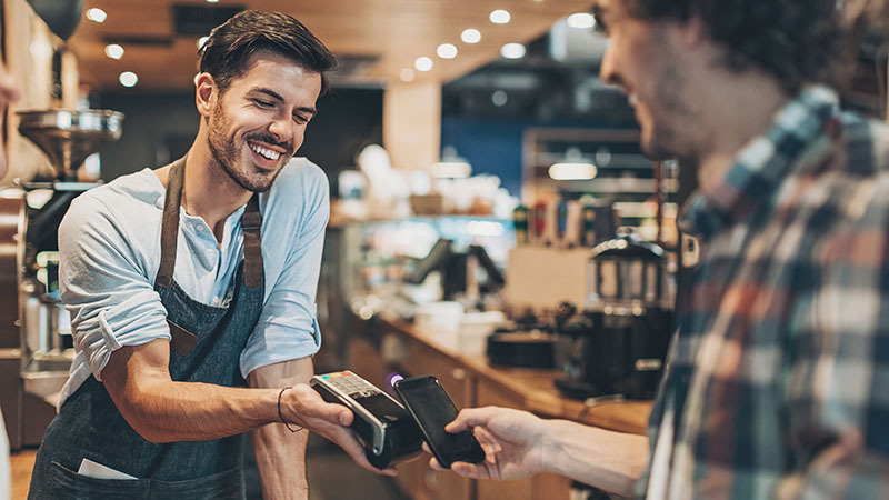 Hombre sonriendo mientras un cliente paga con su teléfono