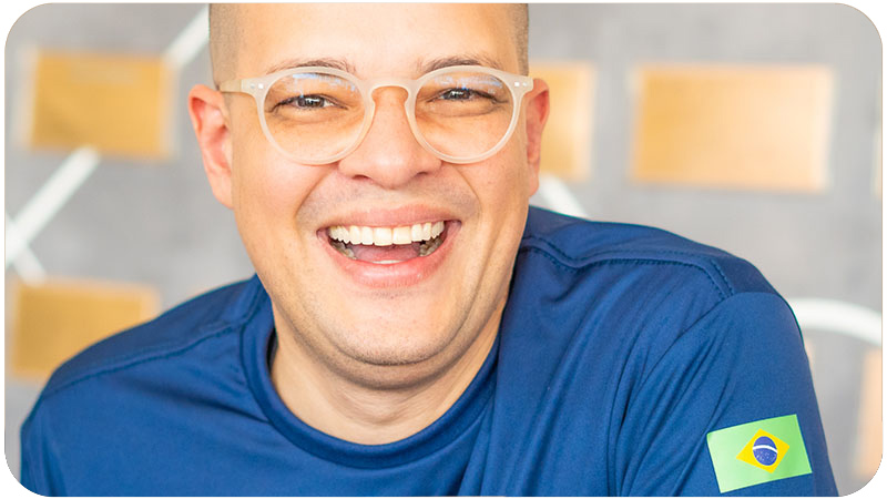 Homem sorridente vestindo uma camiseta azul com detalhes da bandeira do Brasil