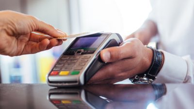 Pessoa pagando com cartão em máquina contactless.