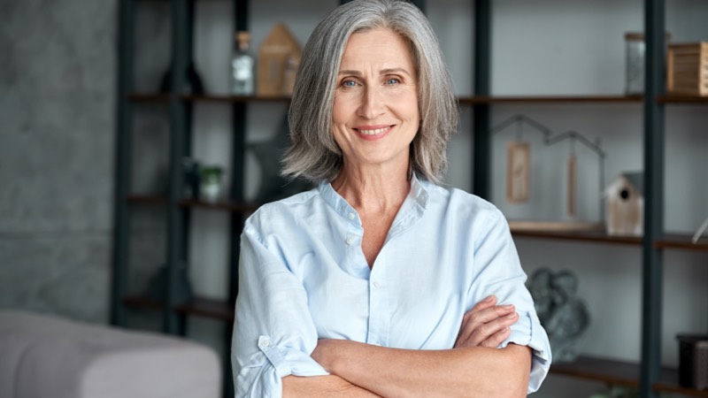 Mulher da terceira idade de braços cruzados sorrindo