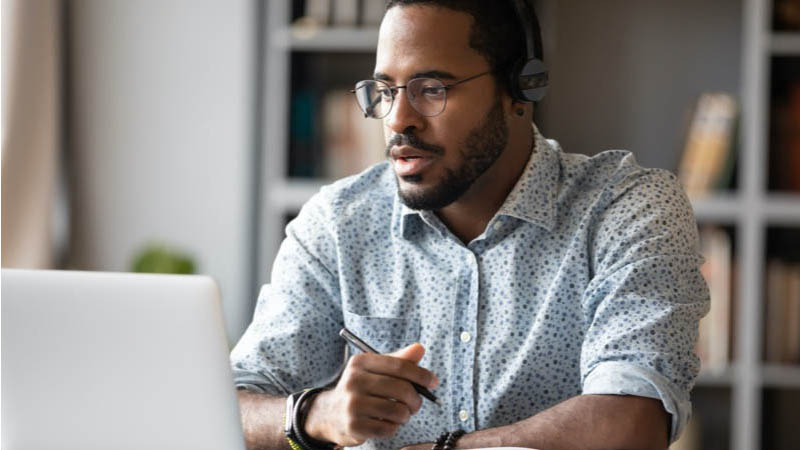 Pessoa com headphones e uma caneta em frente ao computador