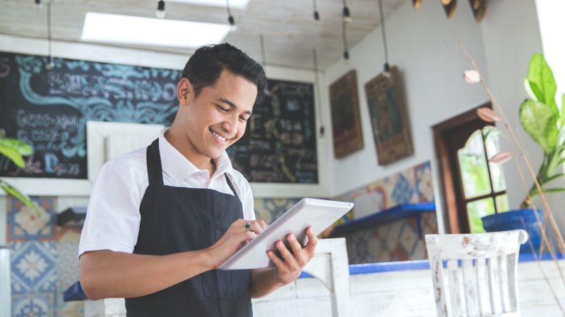 Homem de avental sorrindo com um tablet na mão