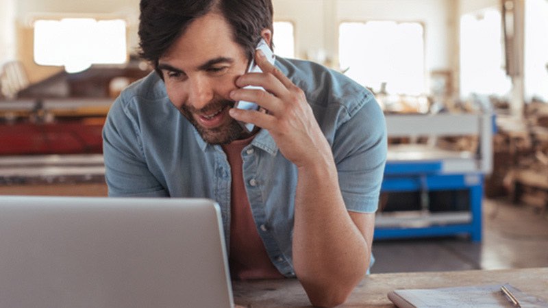 Man looking at laptop while talking on cellphone.