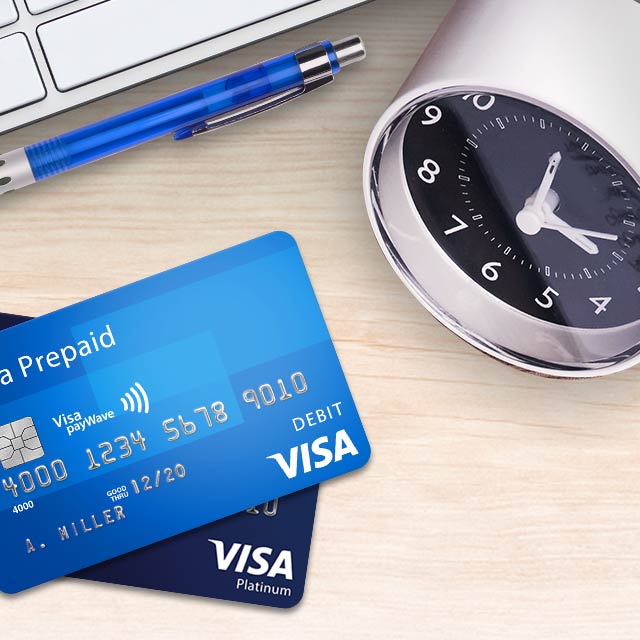 A clock, pen, and a Visa Contactless Prepaid card on a desk.